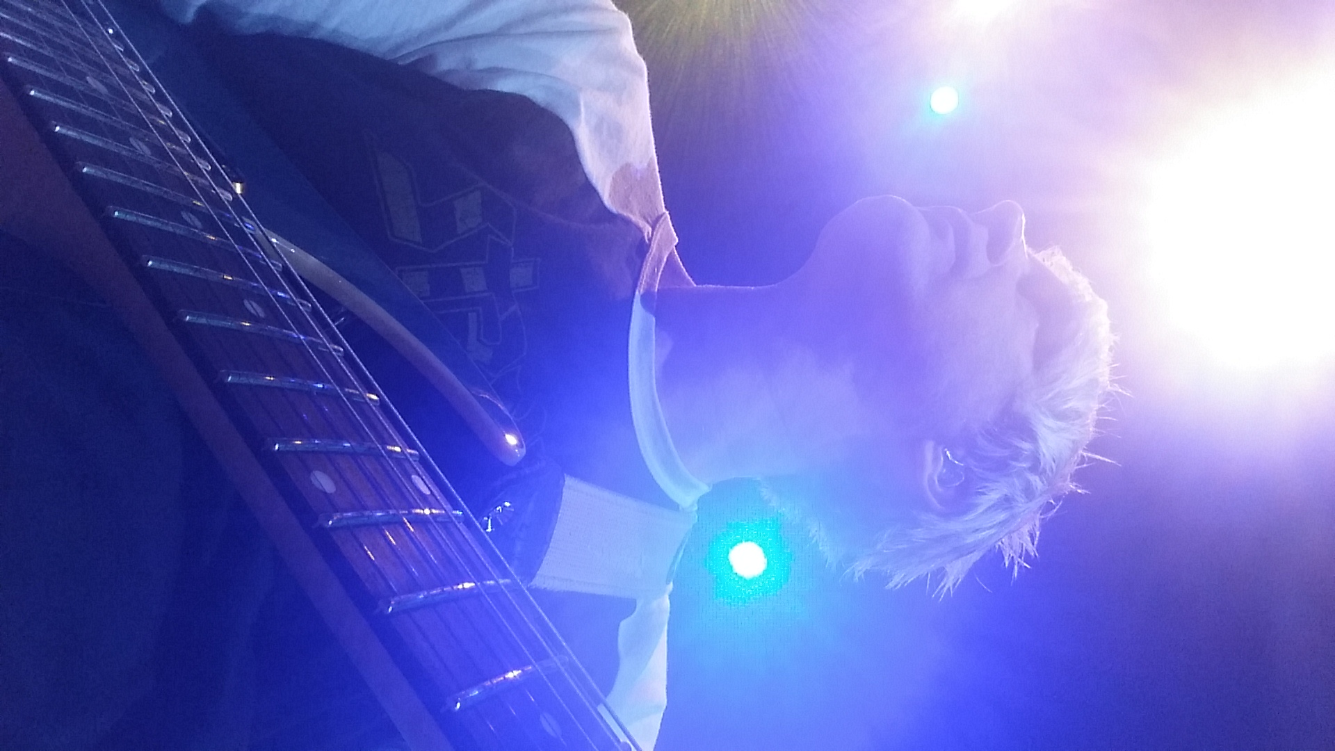 Close-up of Scott Sanford with guitar under blue stage lights