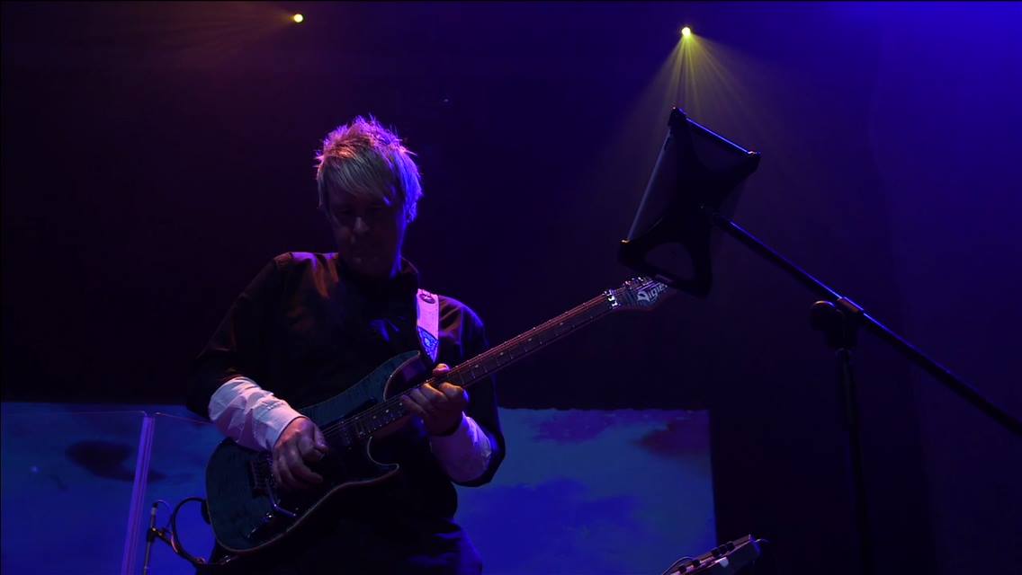 Scott Sanford playing guitar on a purple-lit stage