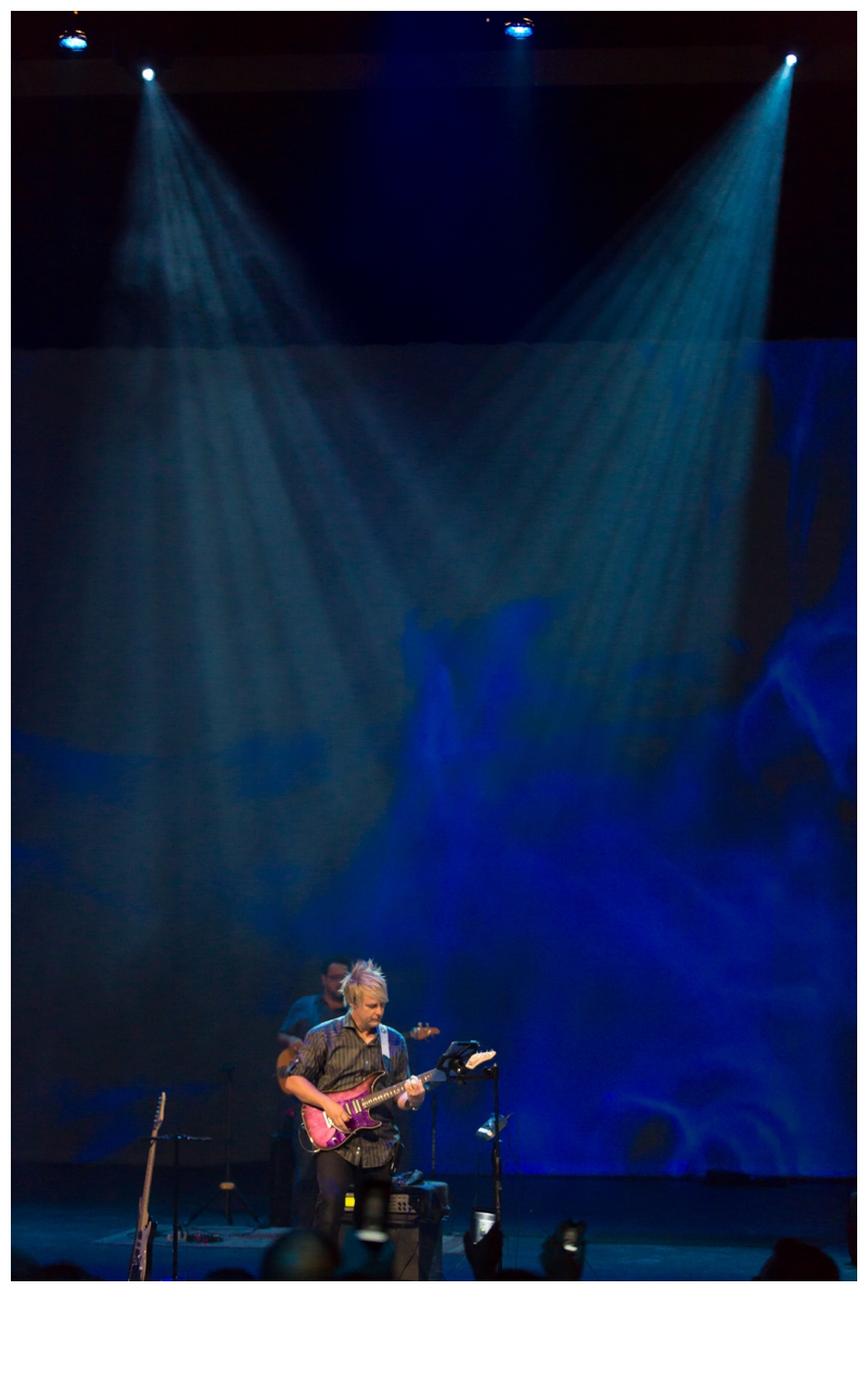 Scott Sanford playing guitar on a wide stage with blue lighting